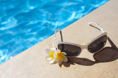 sunglasses-and-white-flowers-of-bougainvillea-near-pool-